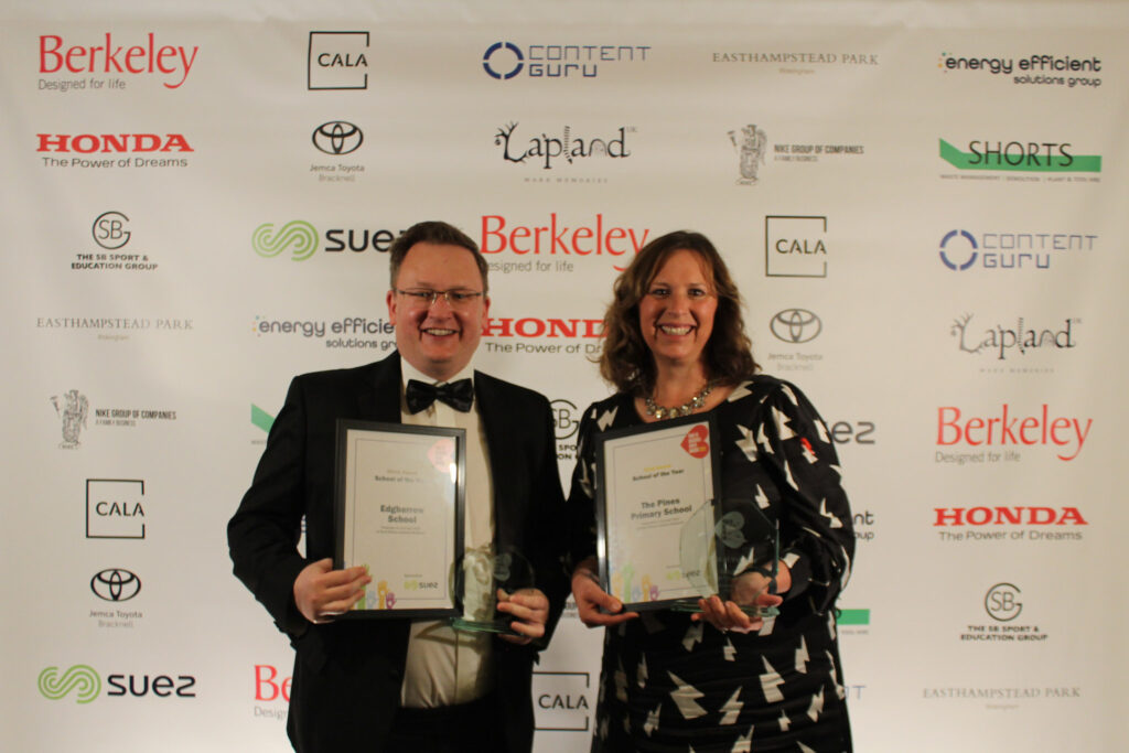 Two winners of an award holding their certificate and trophy in front of the press banner