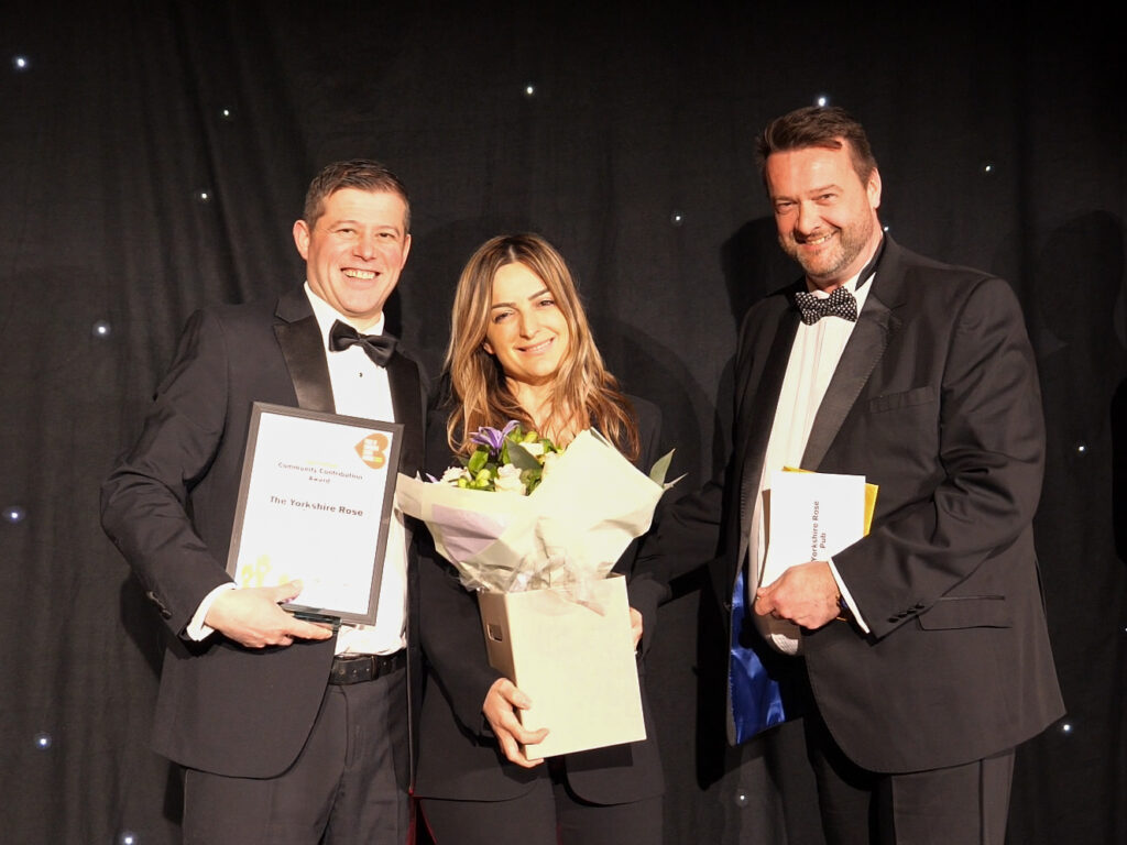 Picture of three individuals on the Pride of Bracknell Forest Awards stage holding their certificate and flowers